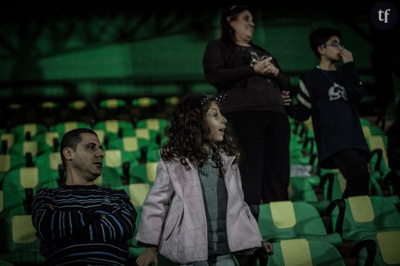 Dans les tribunes du stade, de jeunes spectateurs assistent au match en compagnie de leurs parents.