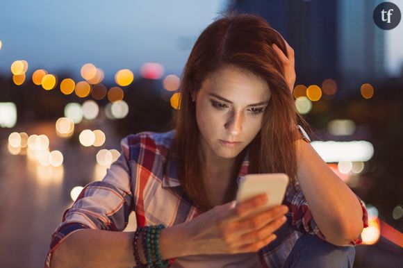 Une jeune femme semble préoccupée devant son téléphone.