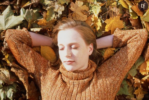 Une femme dort allongée sur le sol recouvert de feuilles mortes.