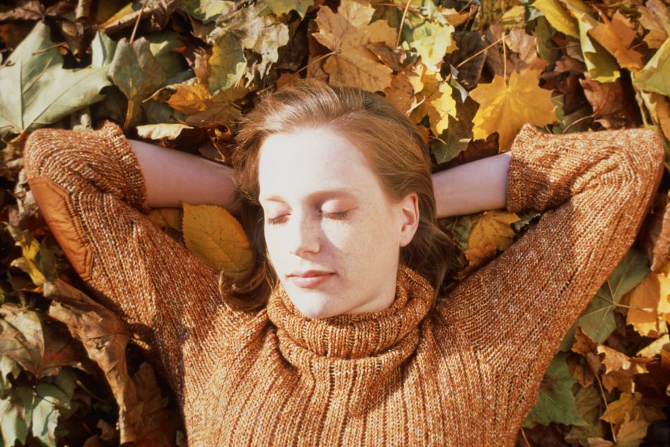 Une femme dort allongée sur le sol recouvert de feuilles mortes.