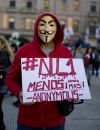 Un homme masqué tient un panneau "Pas une de moins. Plus jamais. Anonymous".