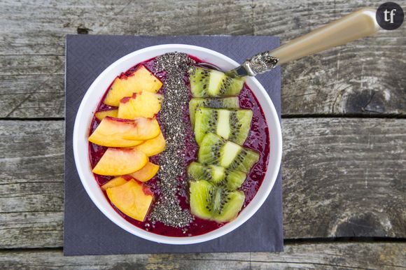 Smoothie bowl sur lit de fruits rouges avec morceaux de kiwi, de pêche et graines de chia