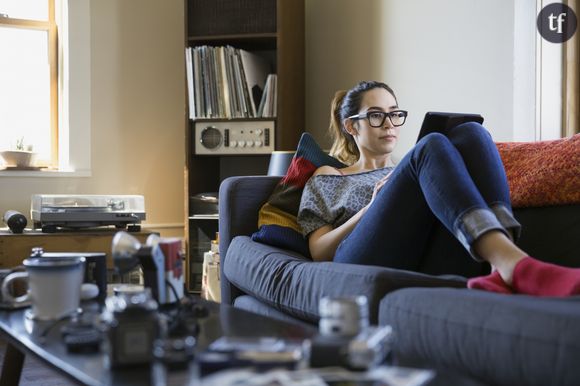 Une jeune femme installée tranquillement sur son canapé avec sa tablette.