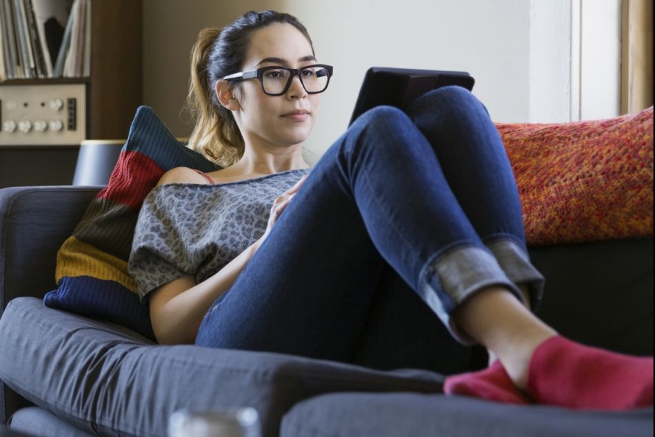 Une jeune femme installée tranquillement sur son canapé avec sa tablette.