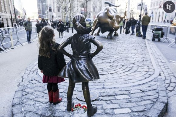 Une fillette posant fièrement à côté de la statue "Fearless Girl".